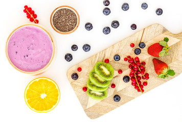 Preparing healthy fruit smoothie. Acai smoothie bowl near cutting board with fresh fruits, berries, chia seeds on white background top view