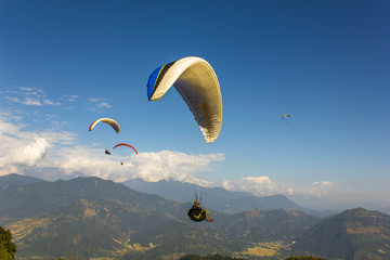 Fototapeta na wymiar paragliders fly over a green mountain valley against a blue sky and white clouds