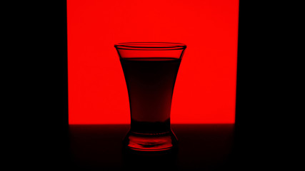 Glass or stemware with alcohol wine,whiskey,gin,beer,rum,vodka,Scotch,cognac,liquor,brandy,absinthe or cocktail on red background. A glass on the bar in a cafe, restaurant, nightclub or disco.