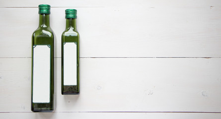 Green bottle for olive oil with white blank sticker for your teat of design. Flat lay, top view with white wooden rustic background. Mock up for product illustration.