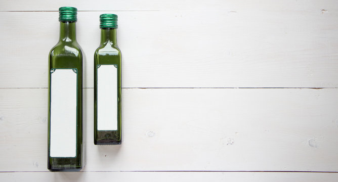 Green bottle for olive oil with white blank sticker for your teat of design. Flat lay, top view with white wooden rustic background. Mock up for product illustration.