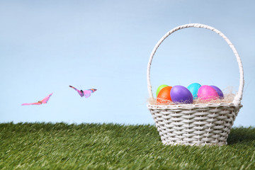 Fototapeta premium Wicker basket full of colorful Easter eggs outdoors on the grass