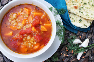 Red lentil soup with sweet potatoes and tomatoes served with naan bread, top view