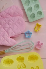 Easter baking.Baking Tools. Silicone Forms with Easter Symbols,  cookie cutters,pink pot holders,kitchen whisk on a light pink wooden background.
