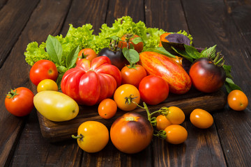 A mix of sliced and whole tomatoes on a rustic wooden board