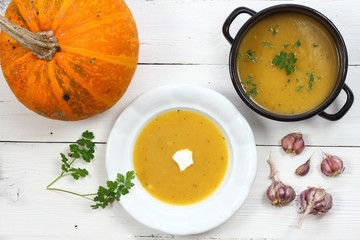 Pumpkin soup in a cooking pot and plate.  Ripe pumpkin and healthy soup with garlic and parsley, flat lay