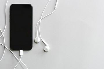 Mobile with black screen and earphone on white table with free copy space.