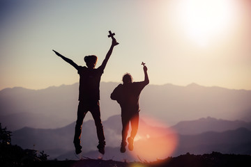 Father and daughter holding a cross are jumping