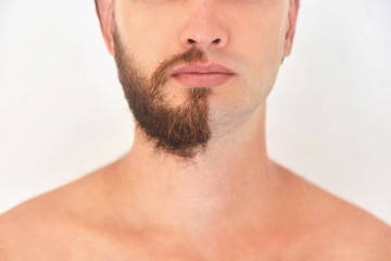 Half shaved. A young man with beard on half of the face on light grey background. 