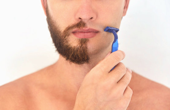 Half shaved. A young man with beard on half of the face on light grey background. 