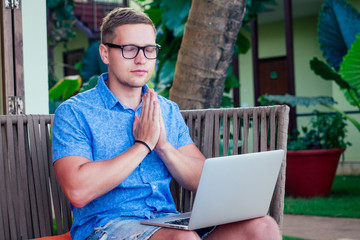 handsome and successful man in a stylish well-dressed freelancer working laptop meditating in the lotus position on the beach.freelance and remote work.businessman namaste and om ocean