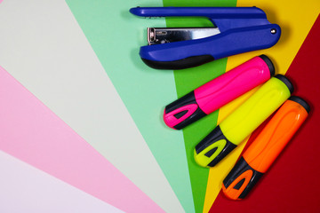 Three color markers and stapler on the colorful background 