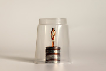 A glass ceiling concept. Miniature women and coins.