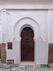 Naklejka premium Traditional Moroccan style design of an ancient wooden entry door. In the old Medina of Marrakech, Morocco. Typical, old, brown intricately carved, studded, Moroccan riad door