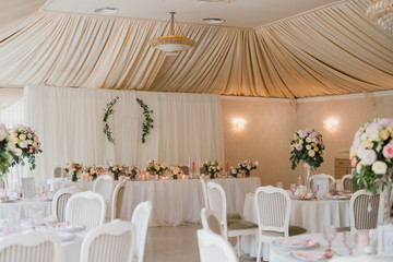 Coziness and style. Modern event design. Table setting at wedding reception. Floral compositions with beautiful flowers and greenery, candles, laying and plates on decorated table.