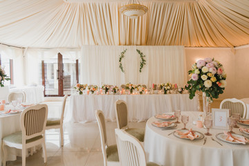 Coziness and style. Modern event design. Table setting at wedding reception. Floral compositions with beautiful flowers and greenery, candles, laying and plates on decorated table.