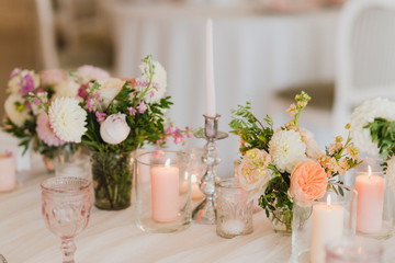 Coziness and style. Modern event design. Table setting at wedding reception. Floral compositions with beautiful flowers and greenery, candles, laying and plates on decorated table.