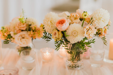 Coziness and style. Modern event design. Table setting at wedding reception. Floral compositions with beautiful flowers and greenery, candles, laying and plates on decorated table.