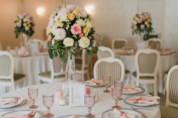 Coziness and style. Modern event design. Table setting at wedding reception. Floral compositions with beautiful flowers and greenery, candles, laying and plates on decorated table.