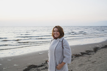 Happy girl walks in a coat along the seashore.