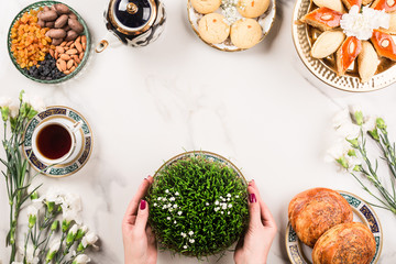 Novruz Azerbaijan traditional table setting, delicious sweet pastry on white background with tea cup, teapot, green wheat grass semeni. Golden plate of pakhlava and shekerbura and gogal, copy space