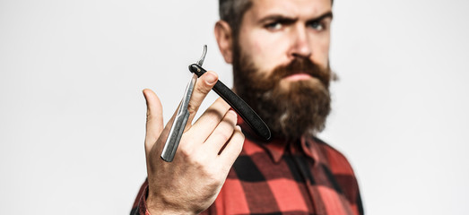 Handsome bearded hairdresser in stylish wear is holding a straight razor while standing at the barbershop. Straight razor, barbershop, beard. Vintage straight shaver. Barbershop service concept.