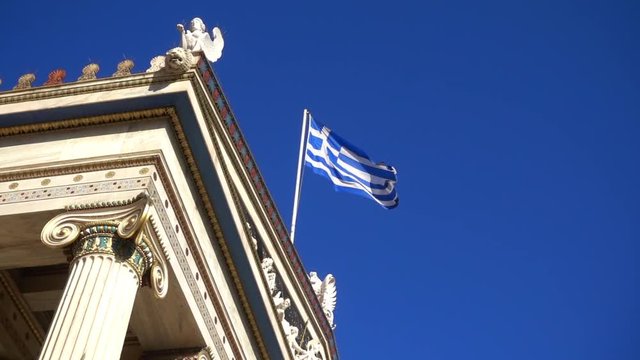 Slow Motion video from iconic neoclassic Academy of Athens facade with Greek flag waving slowly, Athens historic center, Attica, Greece        