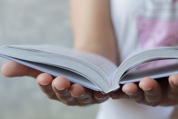 women's hands holding a book in expanded form on a concrete background, the concept of education, knowledge, learning