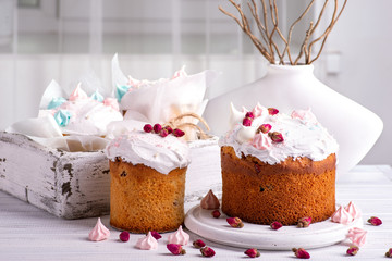 Tree tasty decorate Easter cakes lie on a round white wooden plate on a   white wooden table.  A tray with cakes and flowers  stand on the table.