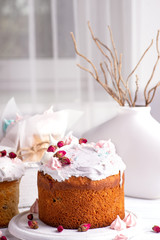 Tree tasty decorate Easter cakes lie on a round white wooden plate on a   white wooden table.  A tray with cakes and flowers  stand on the table.