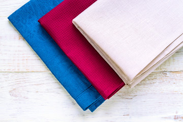 Top view of cloth napkins of beige, blue and burgundy colors on rustic white wooden background.