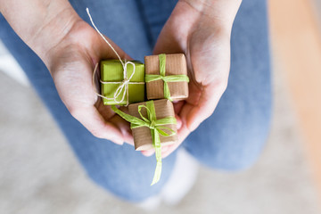 Schenken - Hände halten Geschenke in neutralen Farben verpackt in Recyclinpapier