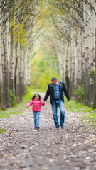 Fototapeta premium The father runs with a daughter and holds her hand on nature on autumn day vacation. Dad and girl walking and playing in the park
