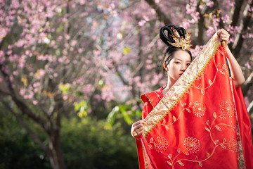 Naklejka premium space beautiful Chinese young woman wearing red traditional cheongsam in cherry blossoms garden