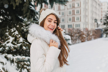 Surprised girl with long straight hair having fun in winter holidays, spending time outdoor. Portrait of enthusiastic caucasian woman in white outfit chilling in park in snowy day.