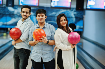Three south asian friends in jeans shirt at bowling club holding balls on hands.