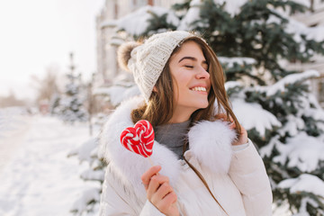 Portrait funny amazing girl enjoying winter time, holding lollypop on street. Brightful happy...