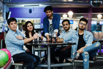 Group of five south asian peoples having rest and fun at bowling club, sitting on table and drinking soda drinks at glass bottles.