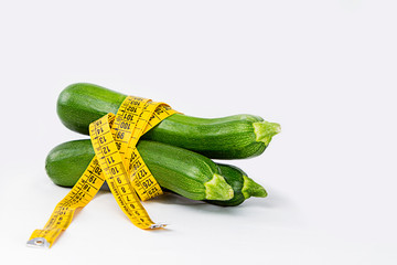 Vegetarian diet to reduce weight. Three freshly picked courgettes wrapped in a body measuring tape ruler that symbolizes the waistline