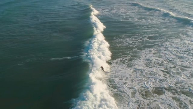 Aerial view slow motion of man surfer with surf board swimming and riding a wave in blue sea ocean