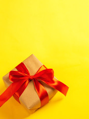 Square gift box with red ribbon on yellow background