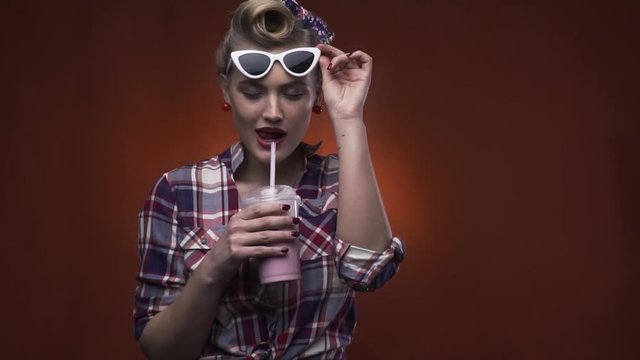 Beautiful vintage blonde girl with white 50s glasses and hairstyle is drinking her milkshake