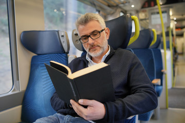 Mature man reading book while traveling on a train