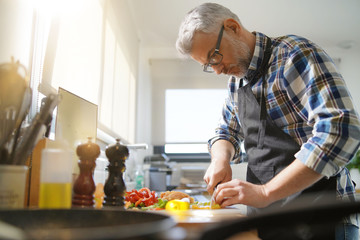 Cheerful mature man in kitchen preparing dish