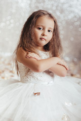 portrait of beautiful smiling little child girl in silver and blue dress on background with silver bokeh. birtday party