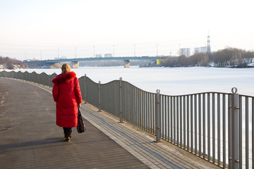 A lonely woman in a red coat walks along the promenade.