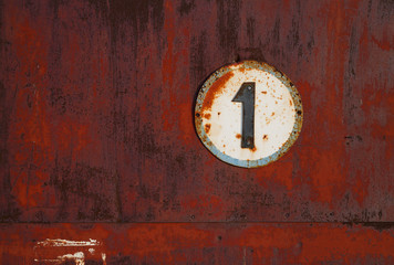 The plate with the number 1 on a rusty metal wall. One on a white circle background. Old uneven iron surface. Perfect for grunge design.