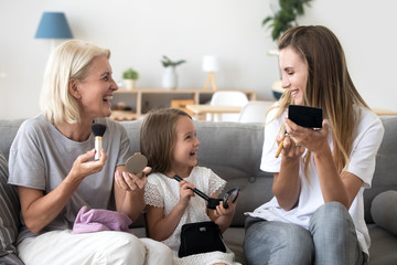 Happy little girl playing with mother and grandmother, doing makeup