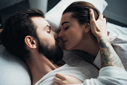 handsome tattooed man embracing beautiful woman while lying in bed