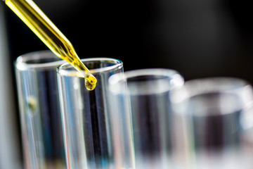 Using dropper sampling oil or chemical liquid drop to test tube with lab glassware in laboratory background, science or medical research and development concept